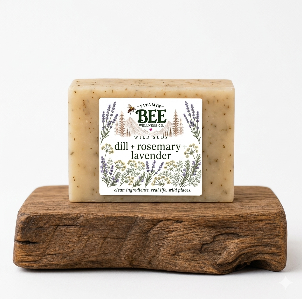 A rectangular bar of Vitamin Bee Wild Rose dill and rosemary + lavender soap, resting on a rustic wooden block against a clean white background.