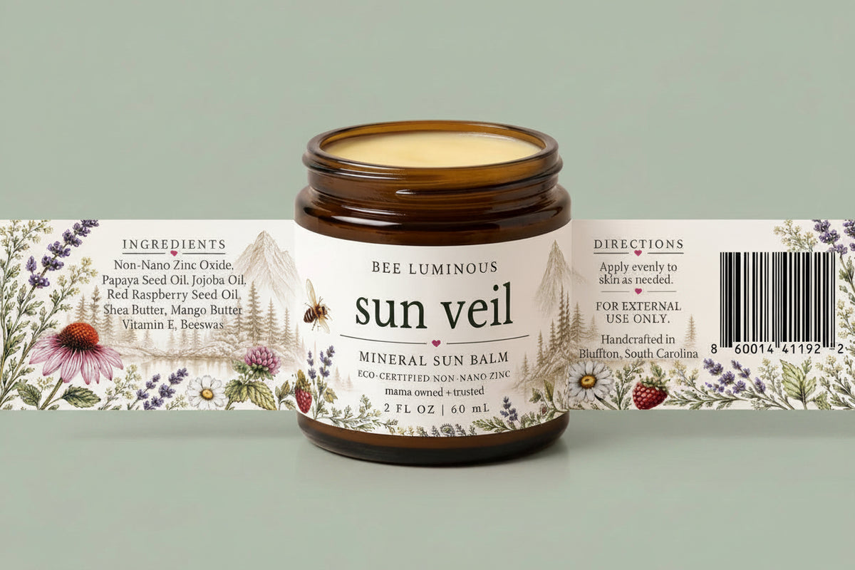 An amber glass jar of Bee Luminous Sun Veil Mineral Sun Balm with a white illustrated label, shown in front of its matching paper sleeve packaging on a light beige background.
