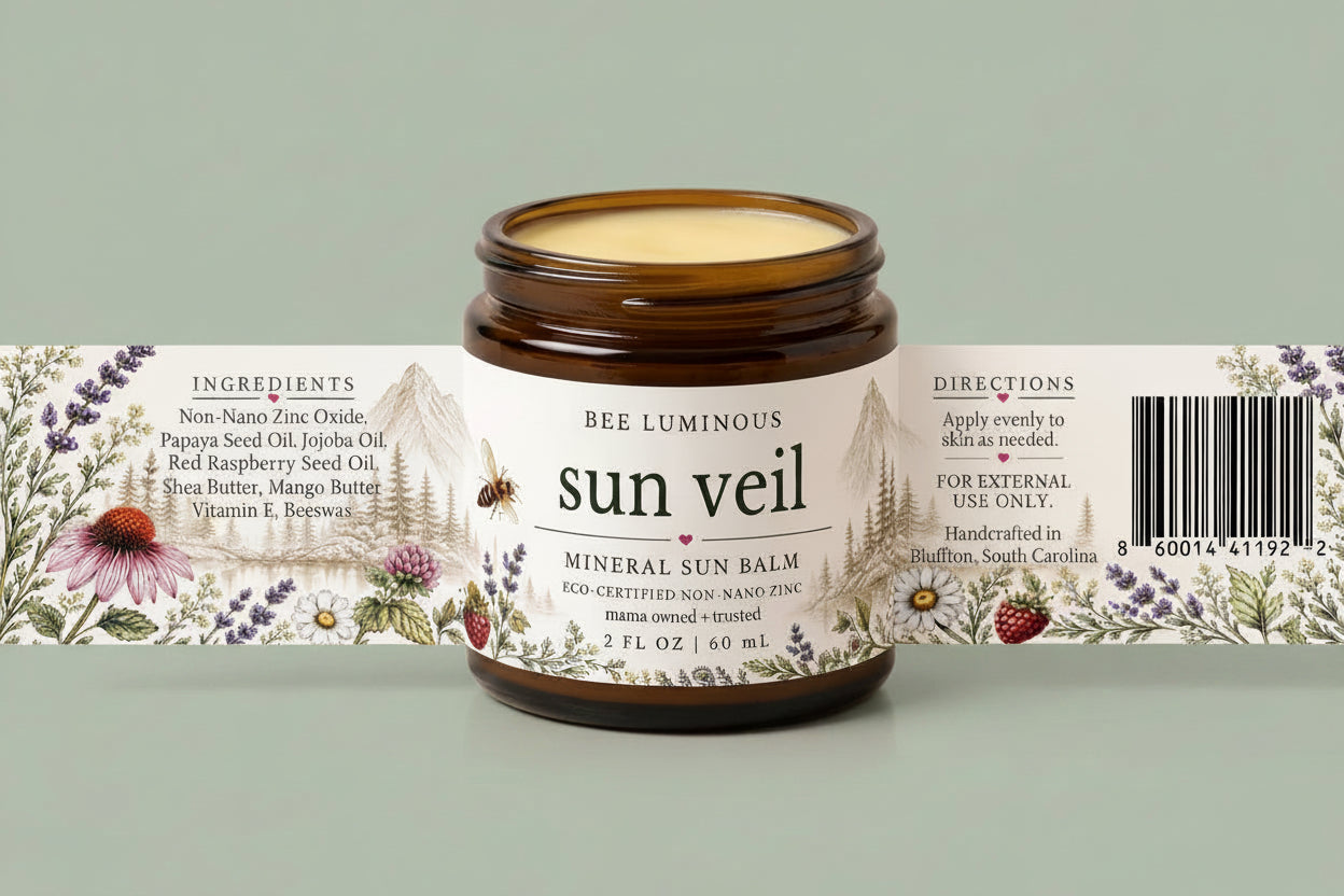 An amber glass jar of Bee Luminous Sun Veil Mineral Sun Balm with a white illustrated label, shown in front of its matching paper sleeve packaging on a light beige background.