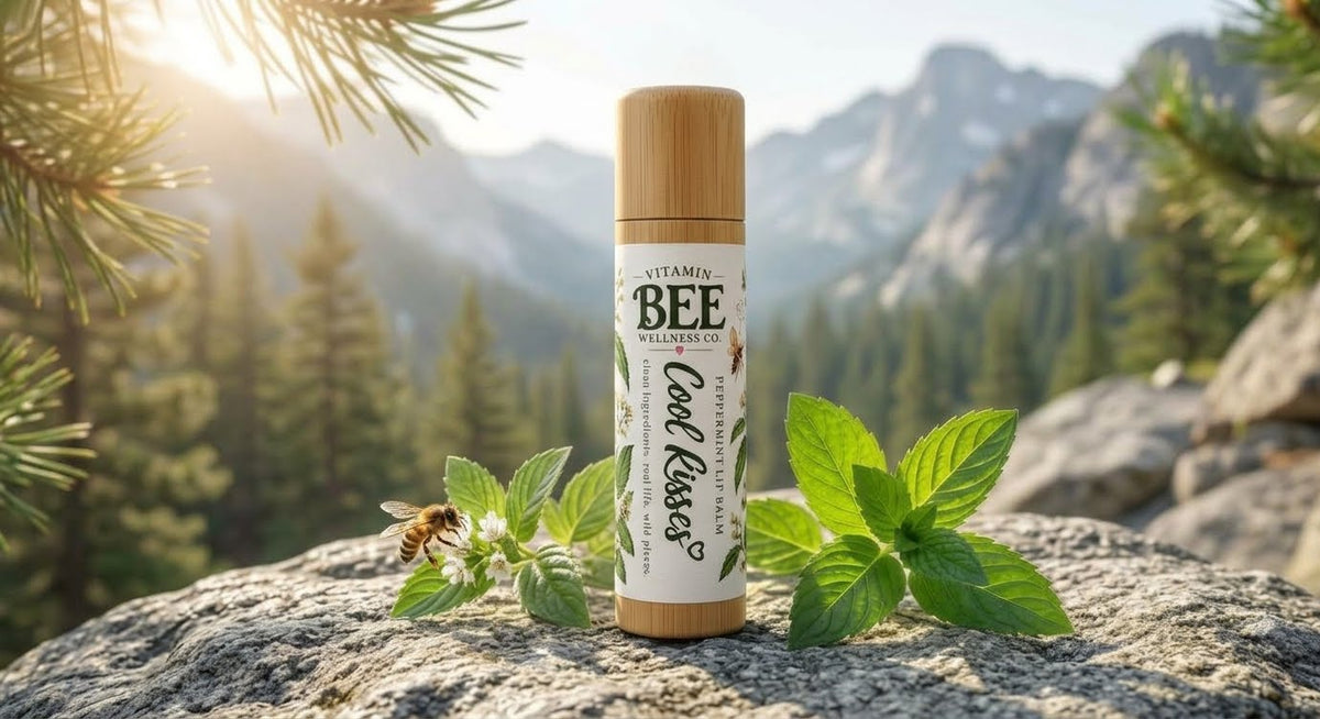 Cool Kisses luxury peppermint lip balm in a sustainable bamboo tube, resting on a granite rock with fresh mint leaves and a honeybee against a sunny alpine mountain wilderness backdrop.